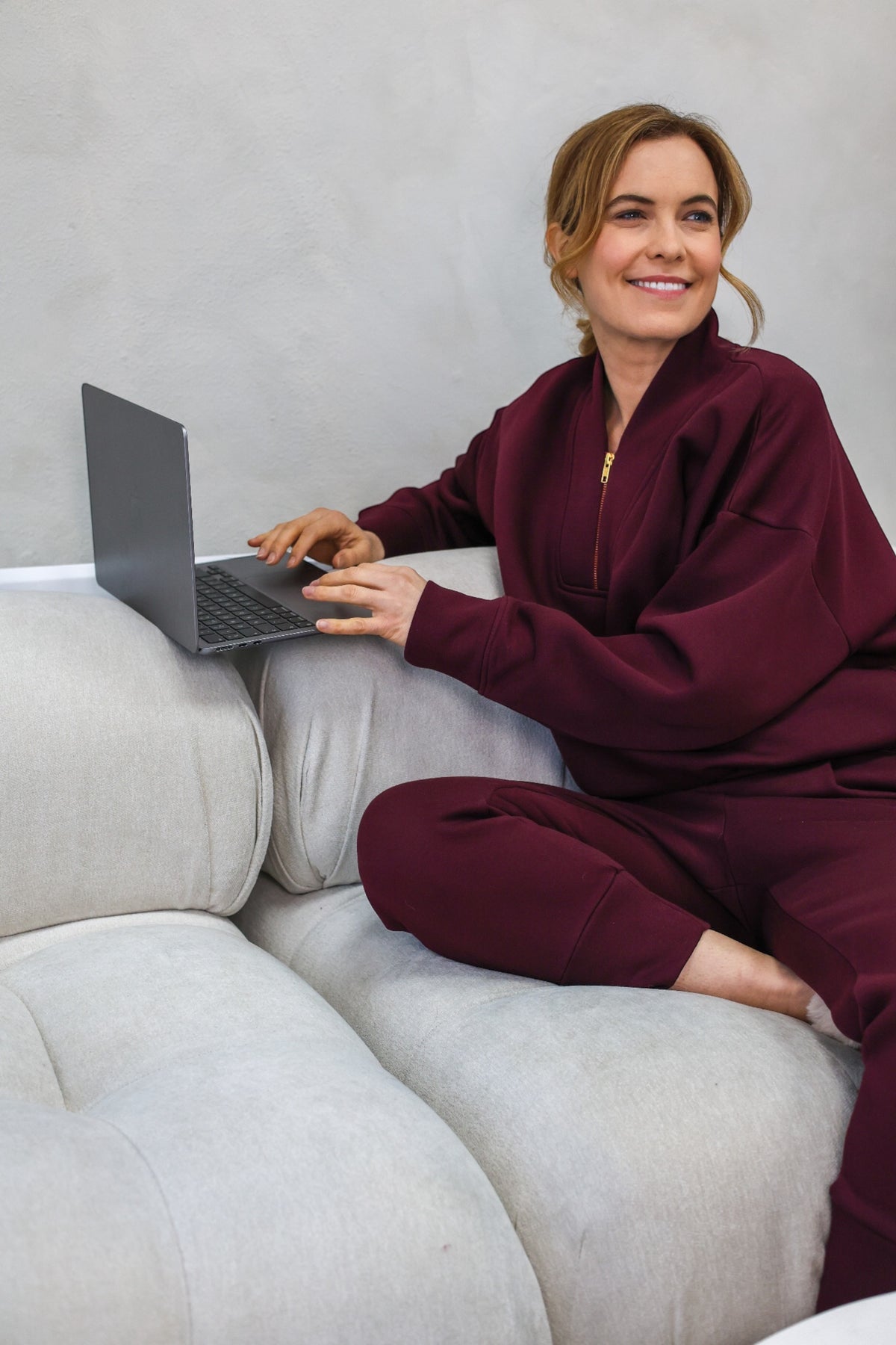 Model wearing a matching burgundy zip-up sweatshirt and jogger pants set against a neutral gray wall.