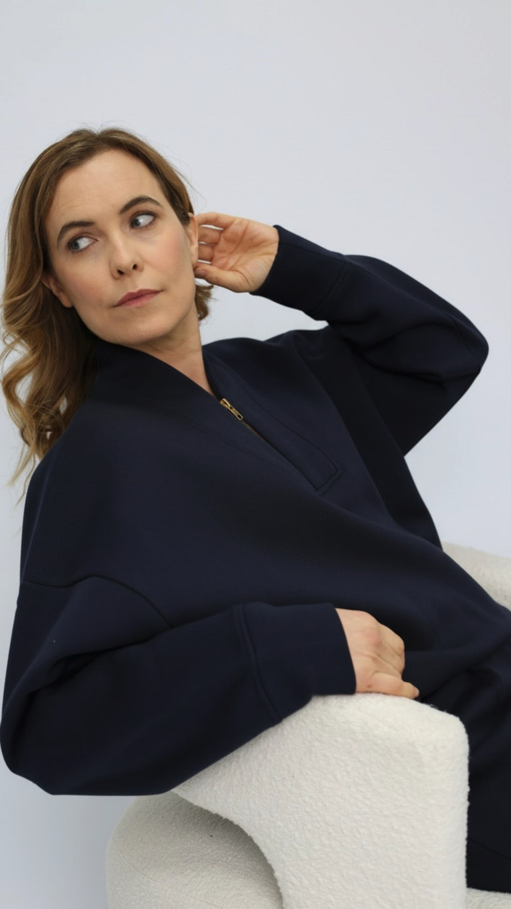 Woman wearing a navy blue sweatshirt sitting on a white chair against a light gray background