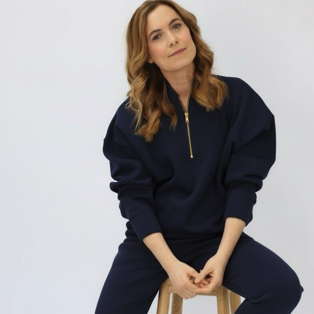 Woman wearing a navy blue tracksuit sitting on a wooden stool against a white background