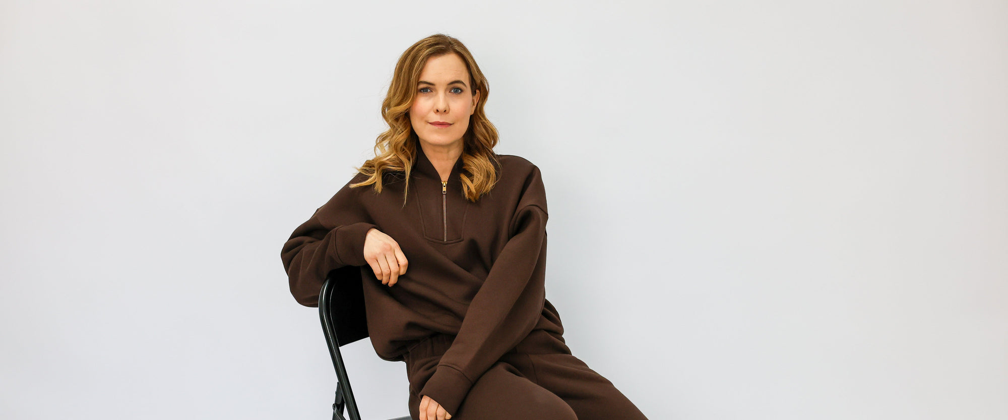 Woman in a brown outfit sitting on a chair against a white background